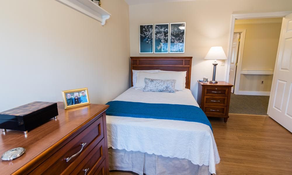 A cozy bedroom with a single bed, nightstand, and lamp, featuring blue accents.
