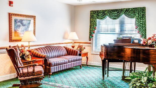 A cozy living room featuring a striped sofa, elegant piano, and a window with decorative curtains.