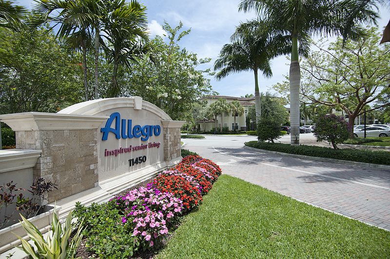 Entrance sign for Allegro, featuring landscaping and flowers with palm trees in the background.