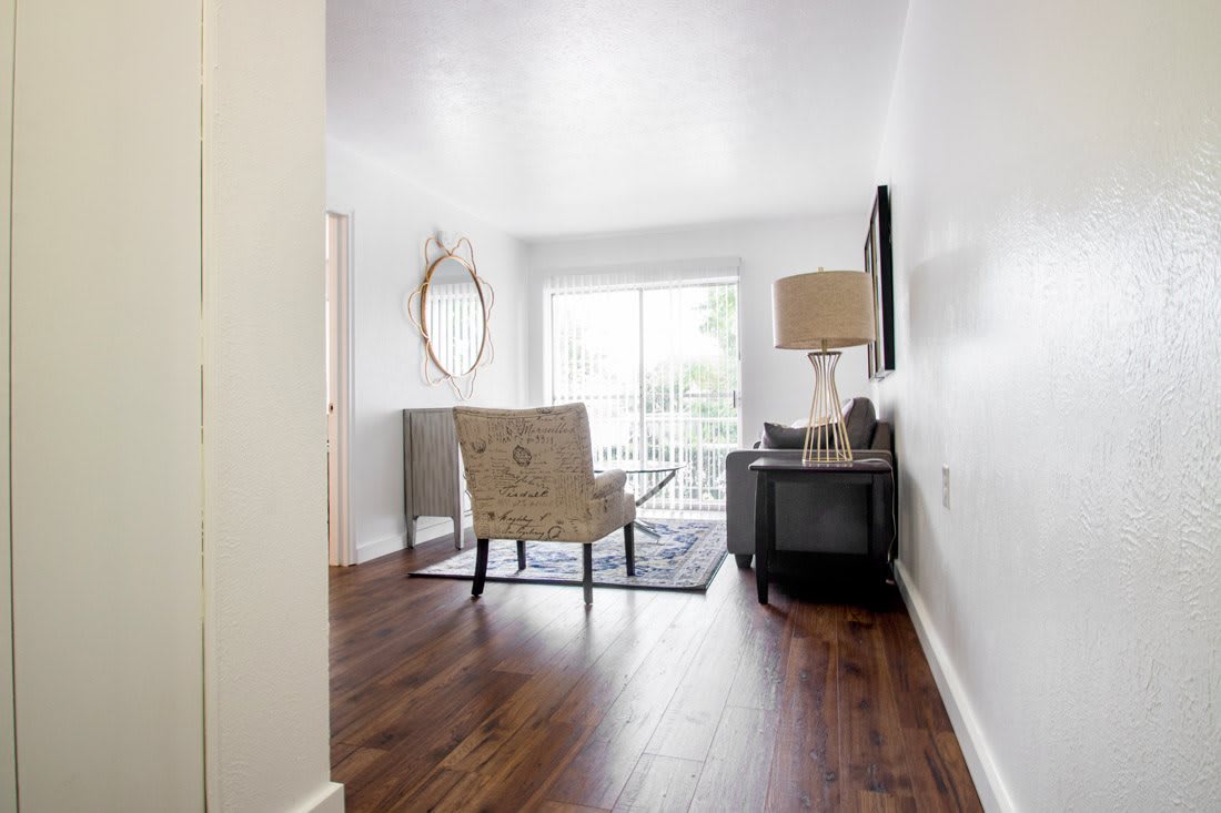 A minimalist living room with a chair, table, lamp, and large window providing natural light.