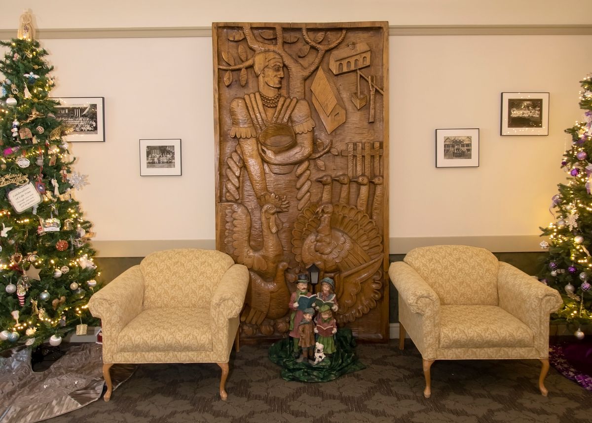 A cozy room featuring a detailed wood carving, flanked by two armchairs with framed photographs on the wall.
