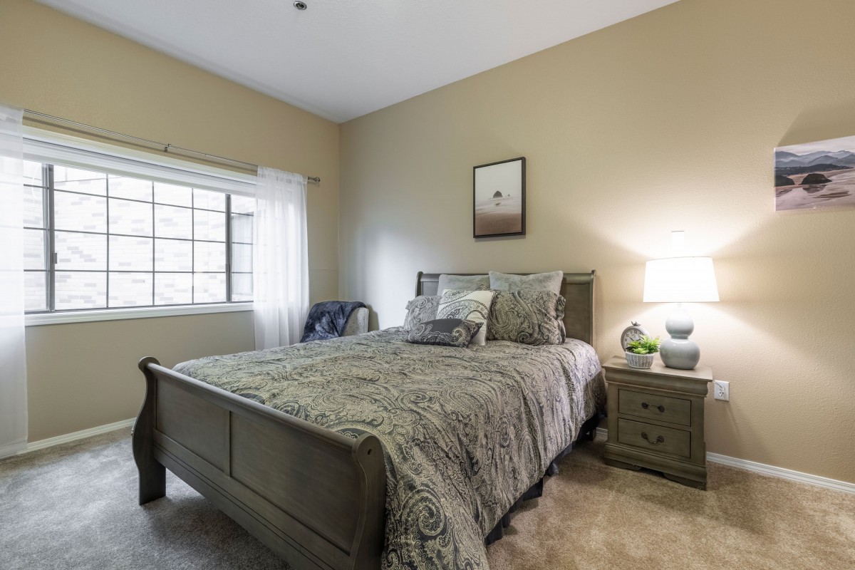 A cozy bedroom with a large bed, nightstand, and lamp by the window.