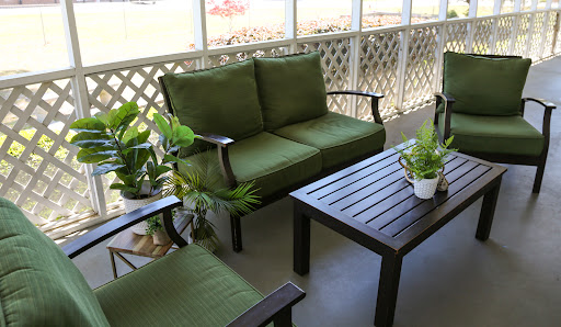 A cozy outdoor seating area featuring a green couch, chairs, and a table surrounded by plants.