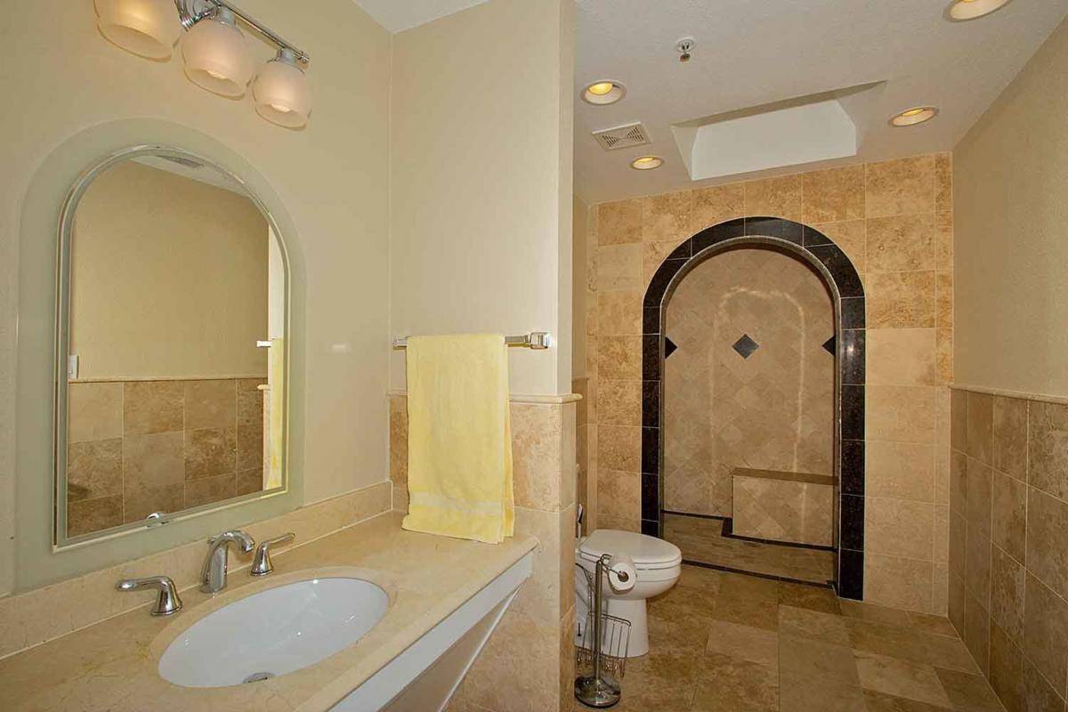 A well-lit bathroom featuring a sink with a mirror, a yellow towel, a toilet, and an arched tiled shower area.