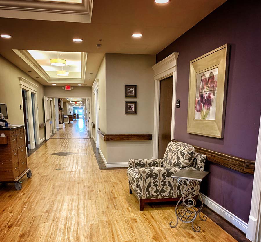 A well-decorated hallway with wooden flooring, featuring a patterned chair and framed artwork on the walls.