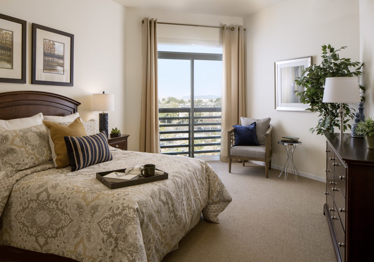 A cozy bedroom with a bed, chair, and a large window overlooking greenery.