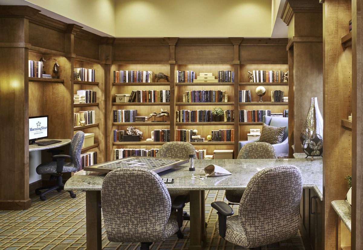 A cozy library interior with bookshelves, seating, and a table.