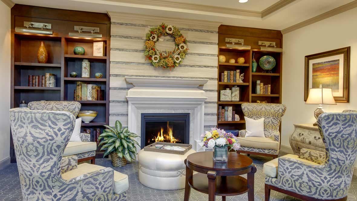 A cozy living room with a fireplace, surrounded by bookshelves and comfortable seating.