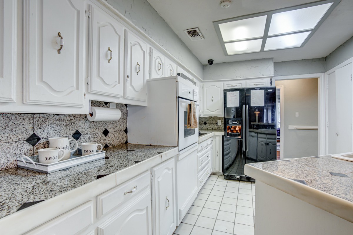 A modern kitchen with white cabinets, a refrigerator, and tiled flooring.