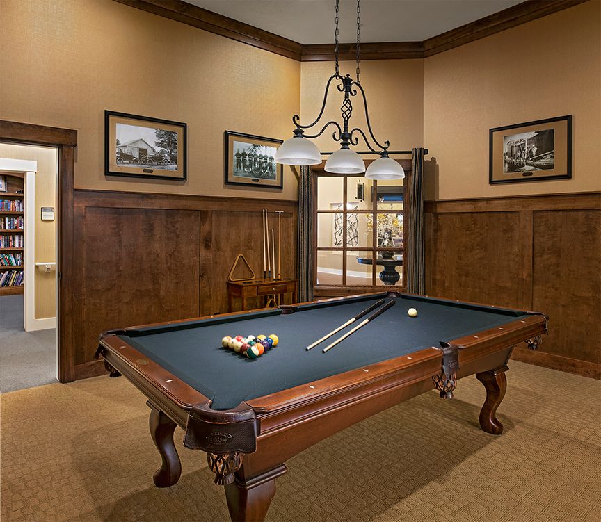 A classic game room featuring a pool table with wooden paneling and elegant lighting.