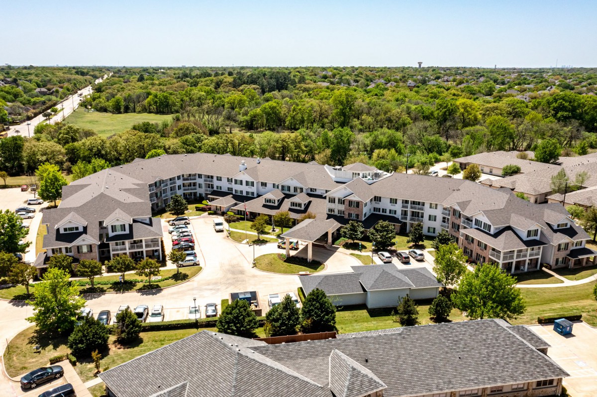 Aerial view of a residential complex surrounded by greenery and a parking lot.