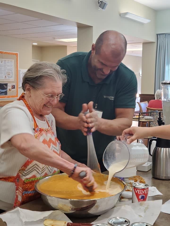 A man and an elderly woman enjoying a baking activity together in a kitchen.