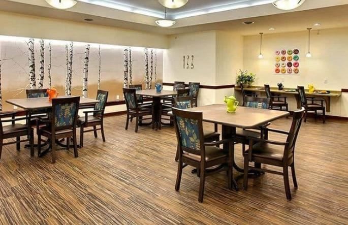 A spacious dining room with multiple tables and chairs, featuring wooden flooring and modern lighting.