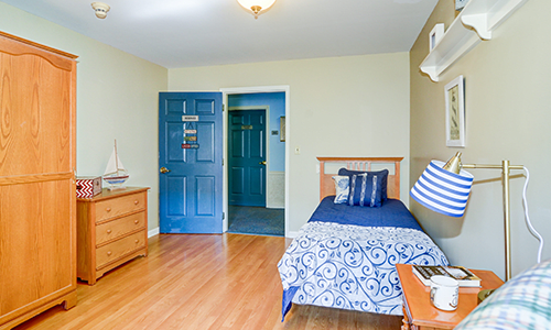 A neatly arranged bedroom featuring a single bed with blue bedding, wooden flooring, and a classic dresser.