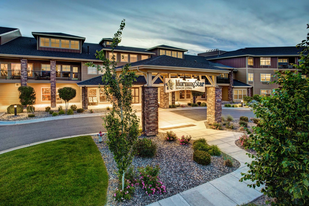 The exterior of a well-lit hotel entrance with landscaped surroundings.