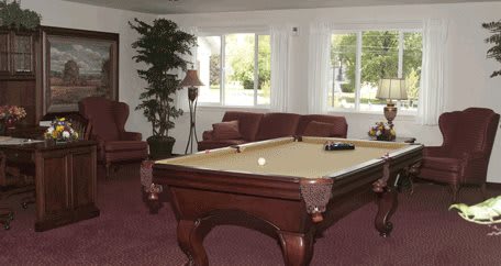 A cozy living room featuring a pool table, comfortable seating, and large windows letting in natural light.