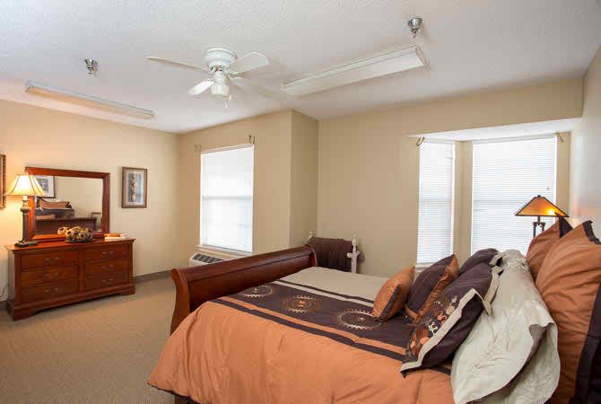 A cozy bedroom with a large bed, ceiling fan, and natural light from the windows.