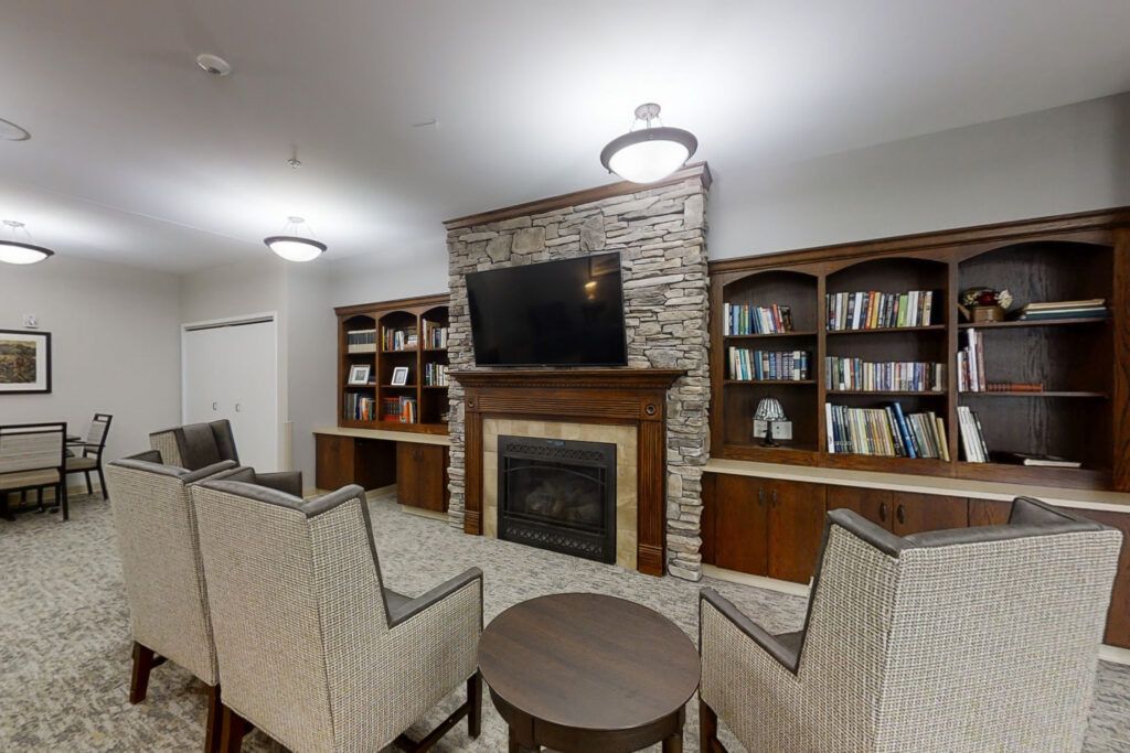 A cozy living room featuring a stone fireplace, built-in bookshelves, and comfortable seating around a central table.