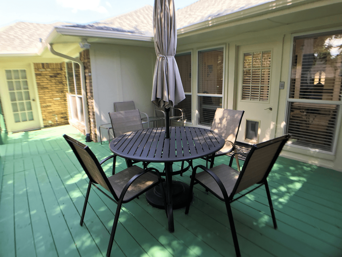 A patio set with a round table, four chairs, and an umbrella on a green deck.