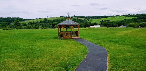 A scenic view of a wooden gazebo surrounded by lush green fields and a winding pathway.