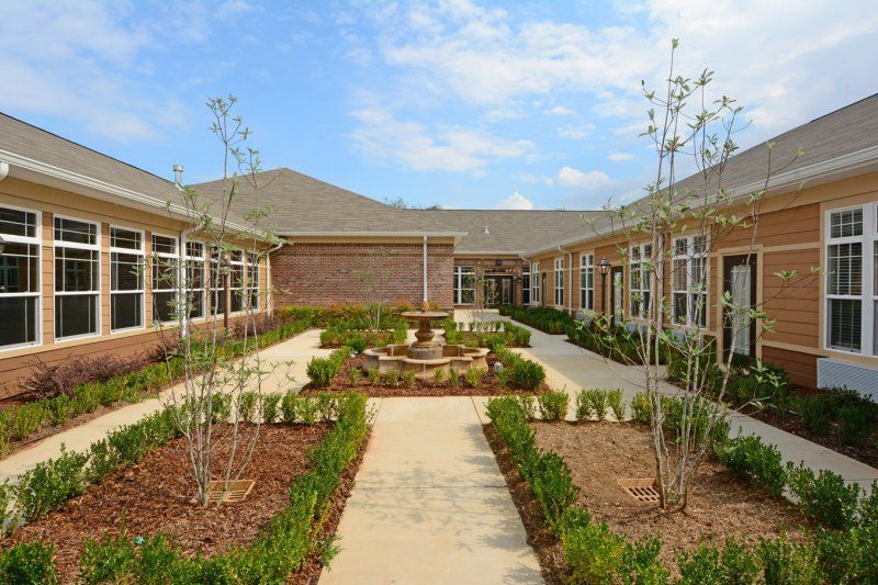 A beautifully landscaped courtyard with a central pathway and a fountain, surrounded by buildings.