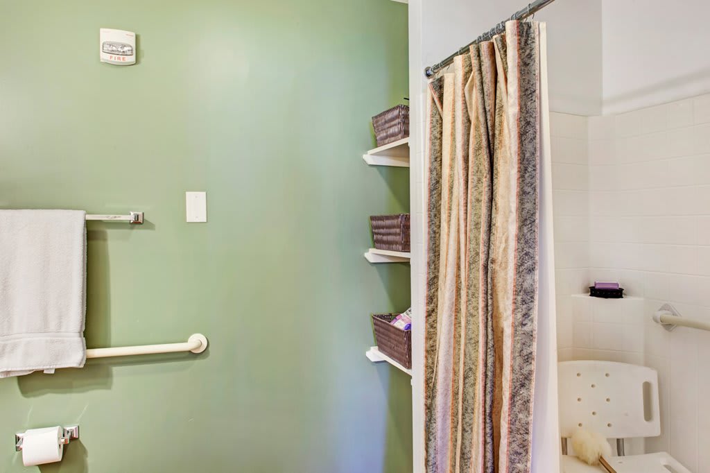 A bathroom featuring a green wall, shower with curtain, and neatly stacked towels on shelves.
