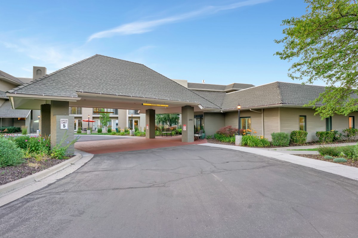 A modern building's entrance with a paved driveway and landscaped surroundings under a clear blue sky.