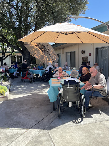 Elderly residents enjoying a lively outdoor gathering under sun umbrellas.