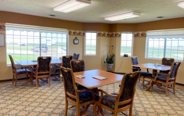 A cozy dining area with tables and chairs, featuring large windows and decorative lighting.