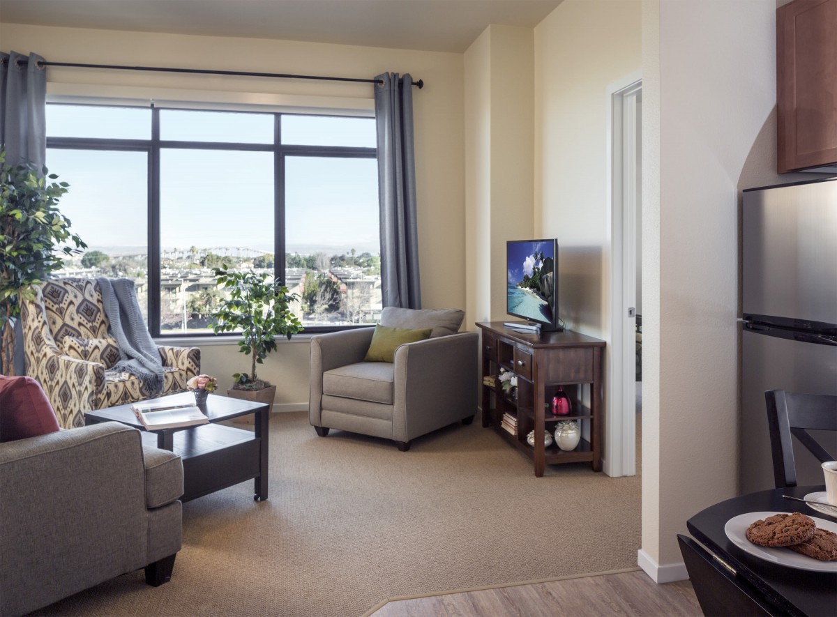 A cozy living room with comfortable seating, large windows, and a television.