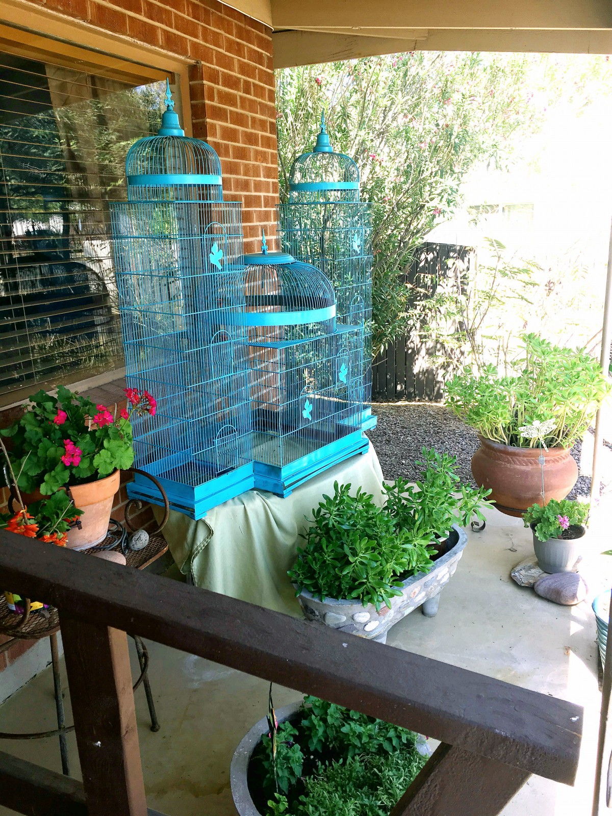A cozy patio featuring a blue birdcage surrounded by vibrant plants and flowers.