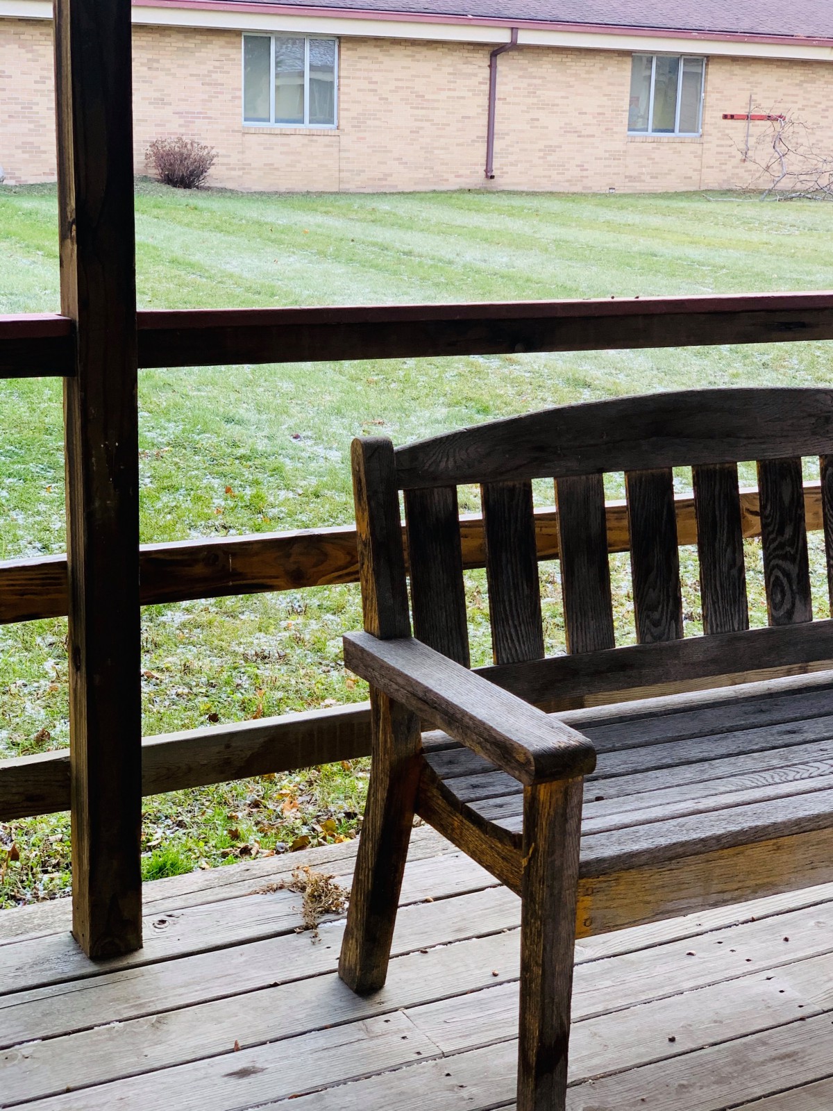 A wooden bench on a porch overlooking a neatly trimmed lawn.