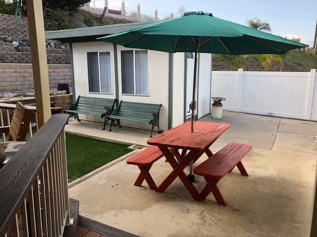 A backyard with a picnic table and umbrella, alongside a swing bench near a small garden area.