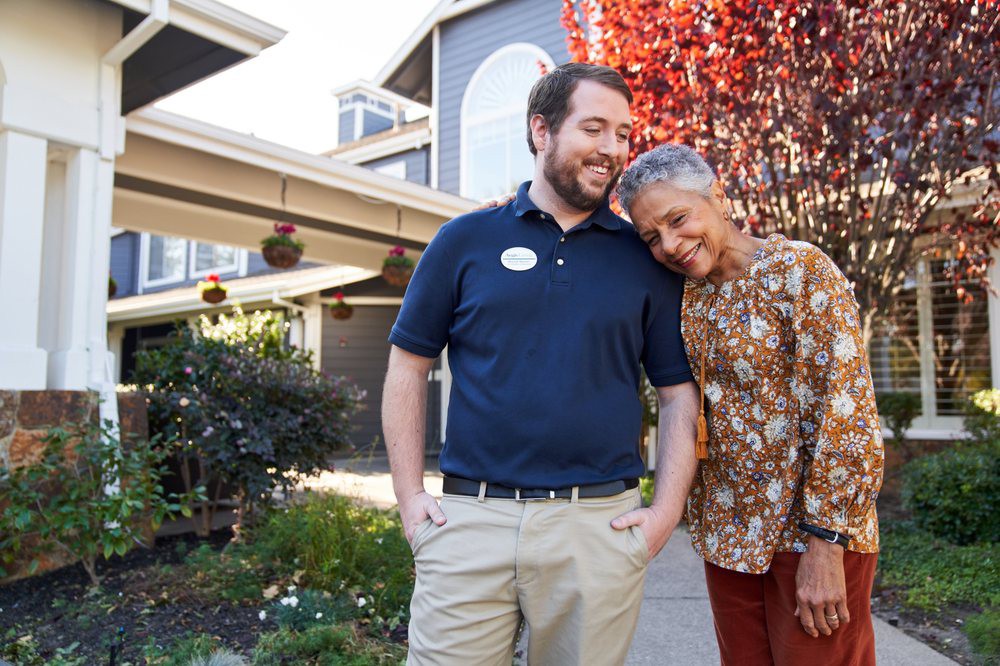 A caregiver and an elderly woman share a moment of companionship outdoors.