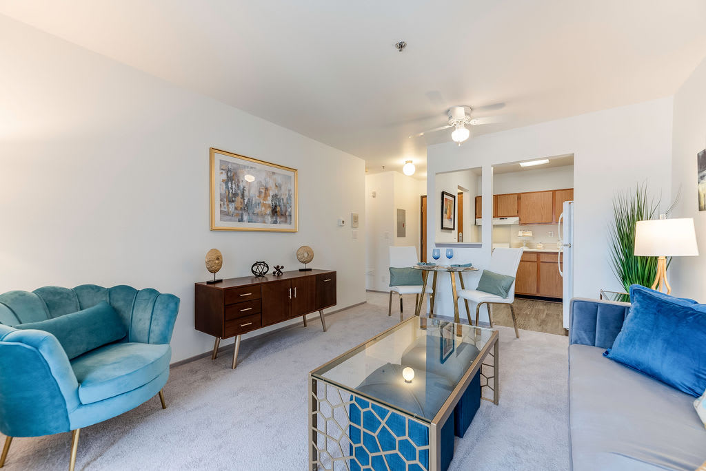 A modern living space with stylish furnishings, featuring blue accents and an open floor plan connecting the living room, dining area, and kitchen.