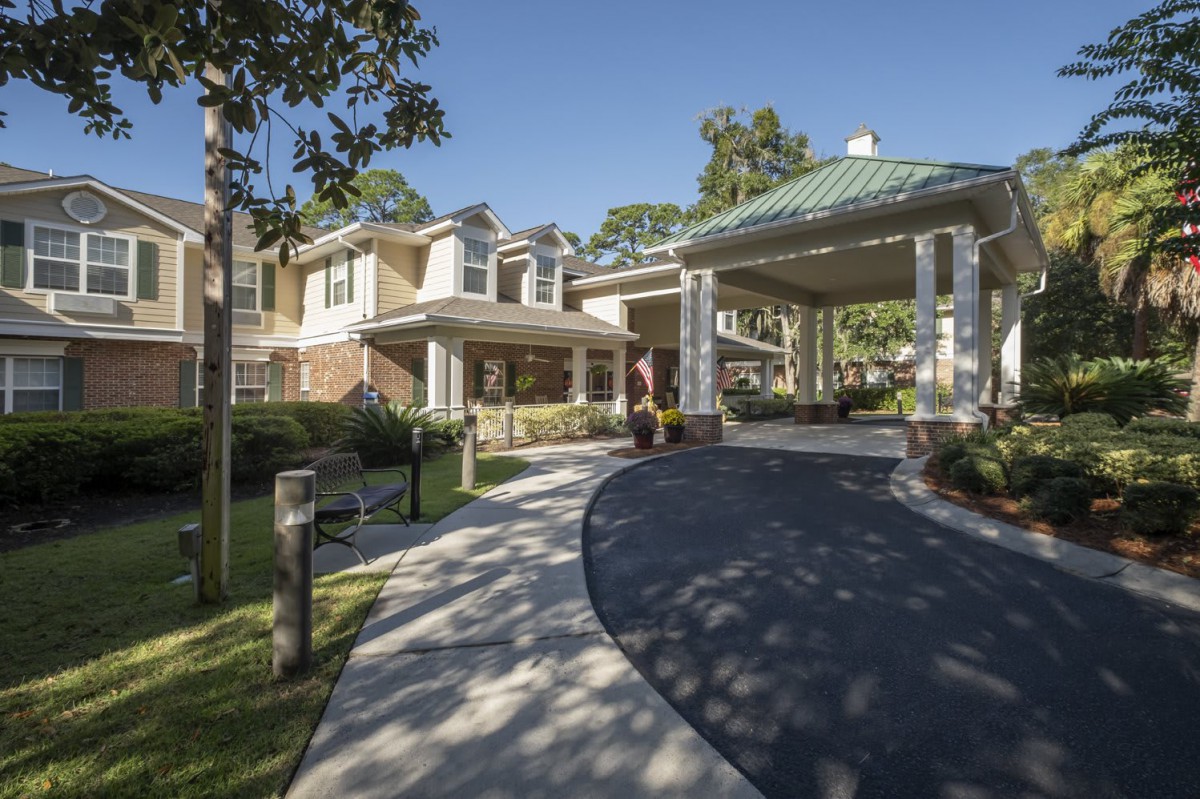 A two-story residential building with a covered driveway surrounded by trees.
