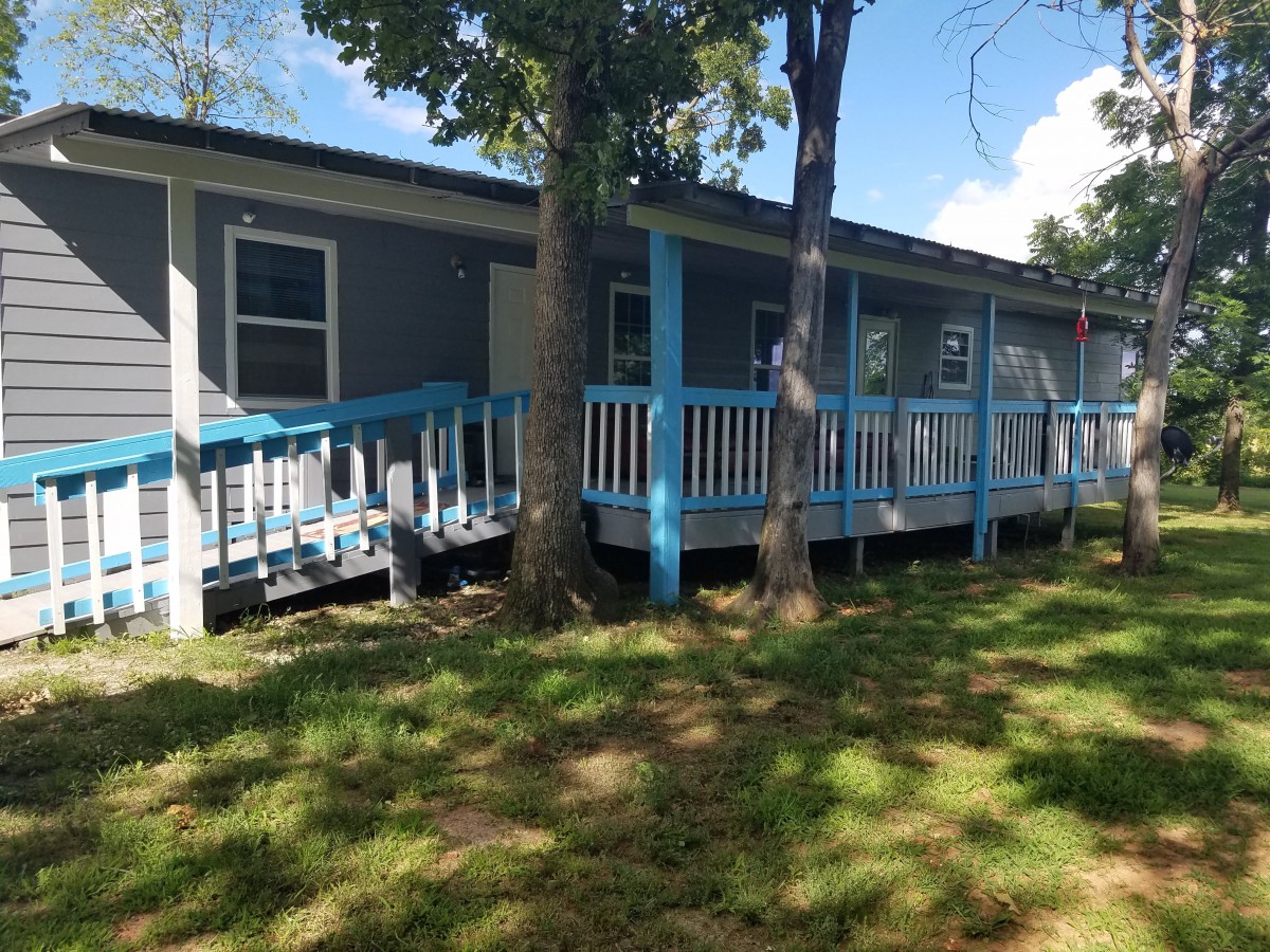 A blue house with a wooden porch surrounded by trees on a sunny day.