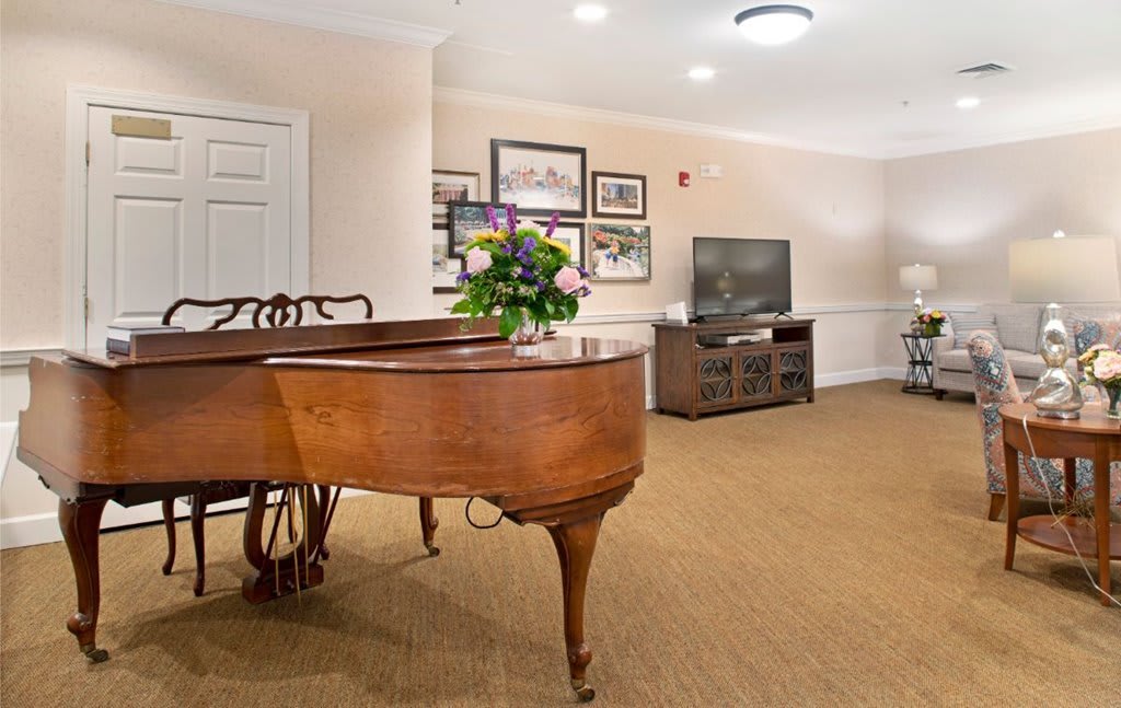 A cozy living room features a grand piano, television, and beautiful floral arrangement.