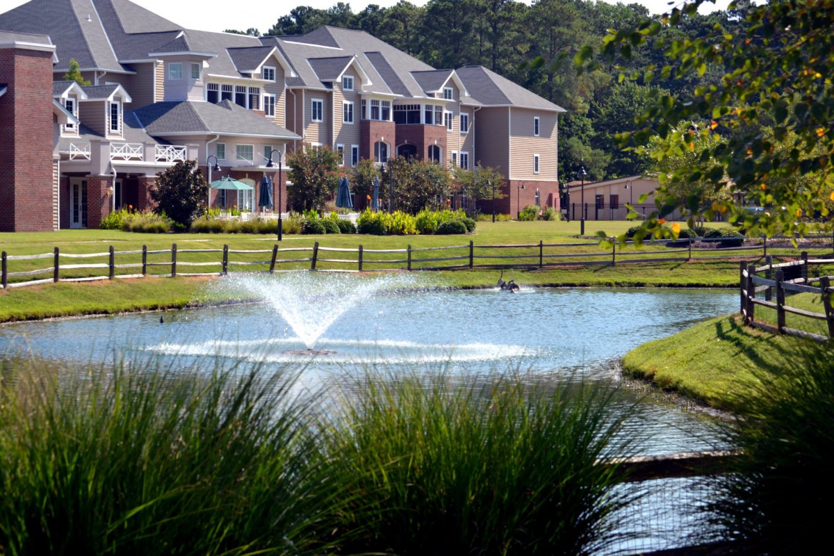 A scenic view of an apartment complex with a pond and water fountain in the foreground.