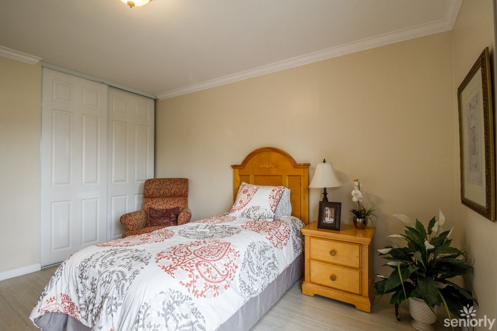 A cozy bedroom featuring a single bed, nightstand with a lamp, and a comfortable chair.
