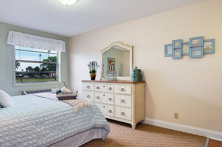 A cozy bedroom featuring a dresser with a mirror, a neatly made bed, and decorative elements near the window.