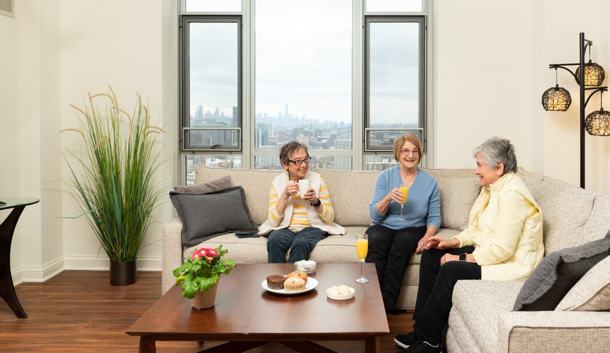 A group of senior adults enjoying a conversation in a cozy living room with a cityscape view.