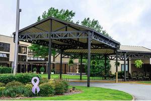 A modern canopy structure in front of a building, surrounded by landscaping and greenery.