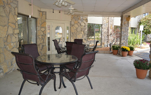 A cozy outdoor seating area featuring a glass table and metal chairs, surrounded by stone walls and plants.