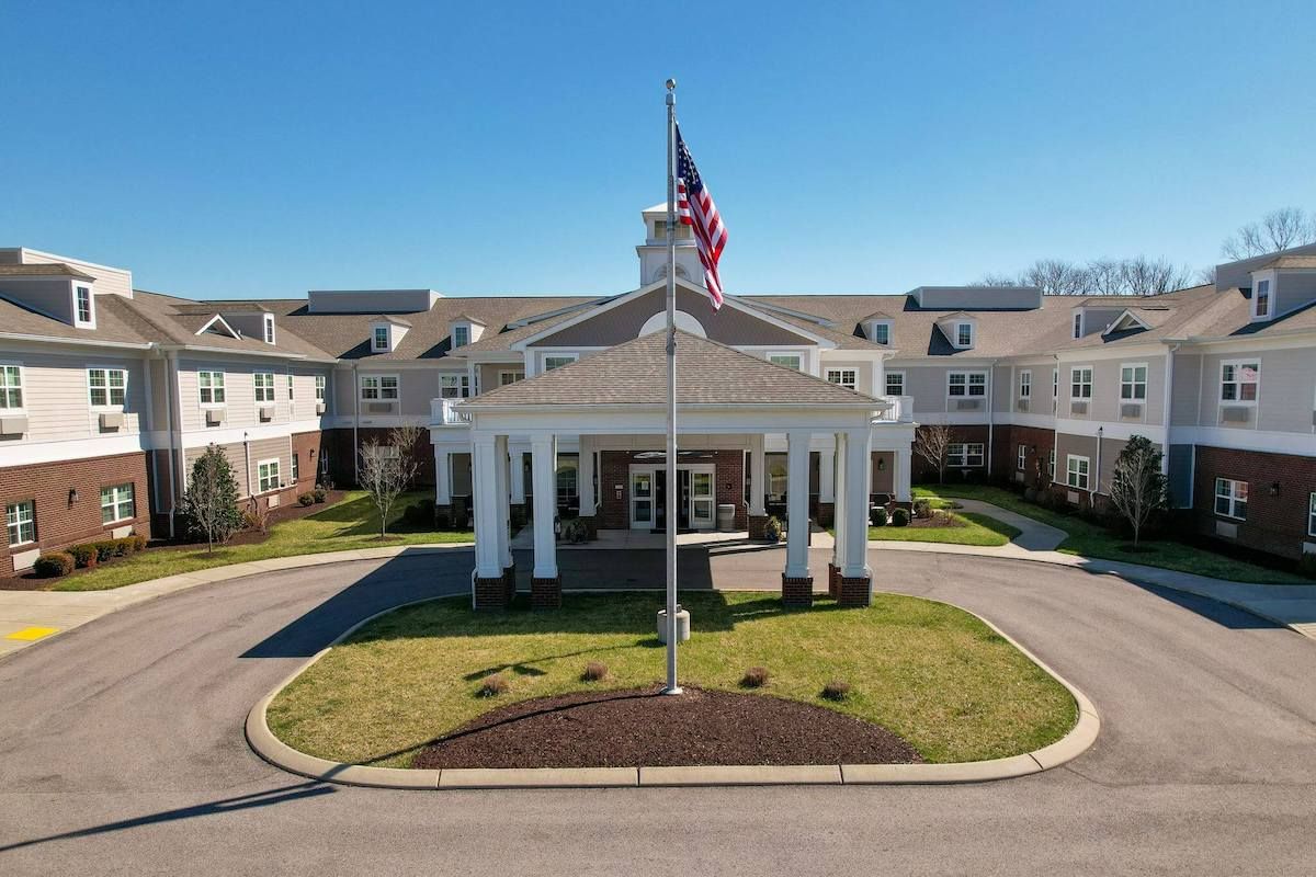 A large residential building with an American flag at the entrance, surrounded by landscaped grounds and a circular driveway.