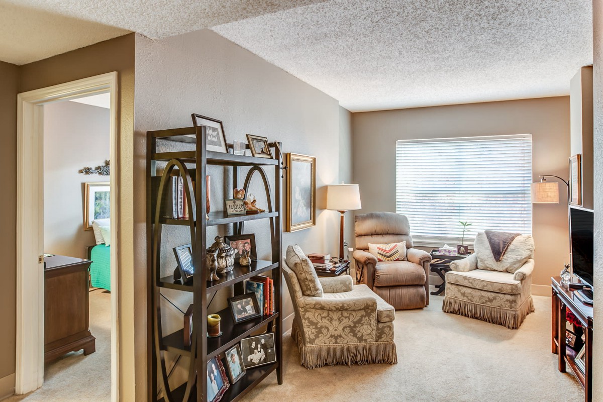 A cozy living room with armchairs, a bookshelf, and a large window letting in natural light.
