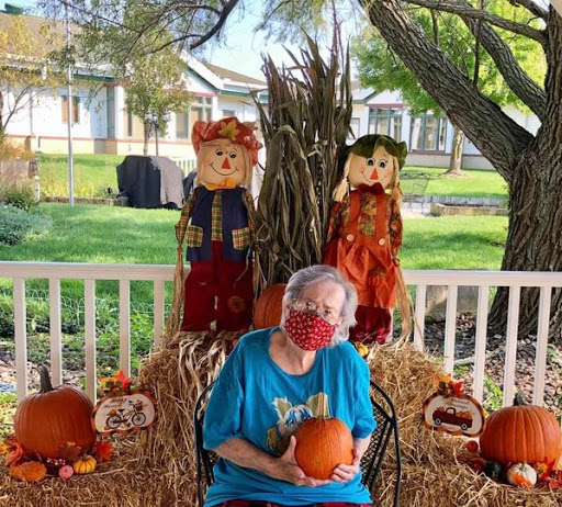 A cheerful autumn scene featuring a senior person seated with pumpkins and festive decorations.