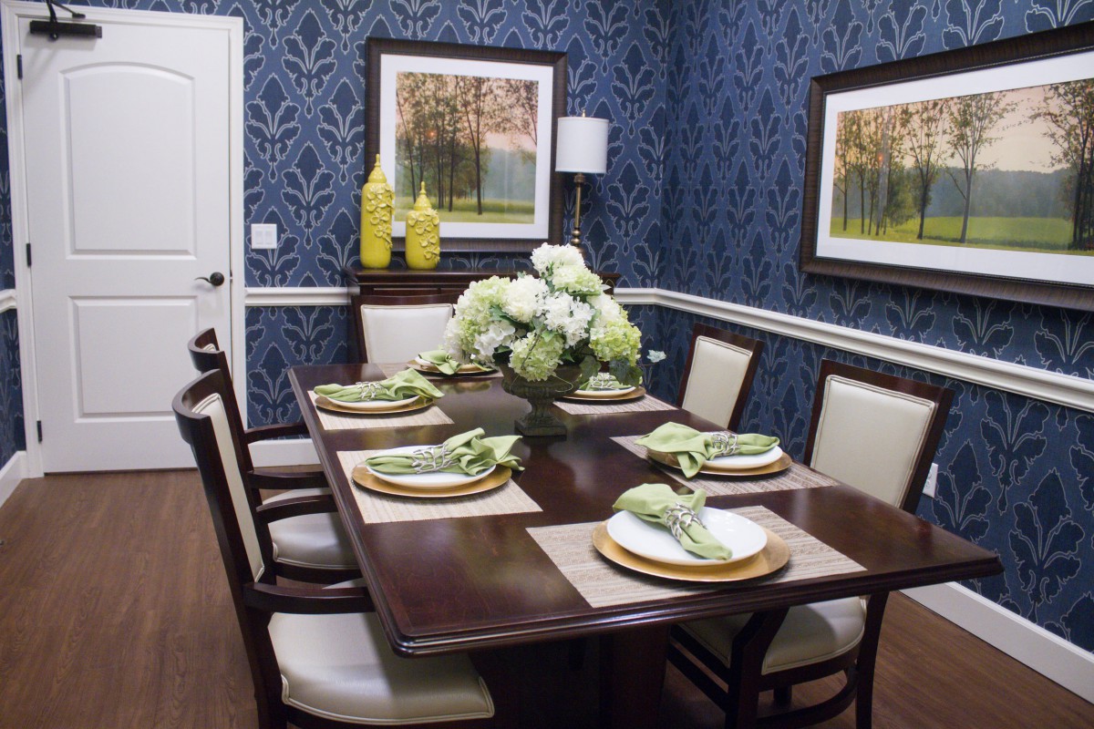 Elegant dining room with blue wallpaper, featuring a dark wood table set with green napkins and floral centerpiece.