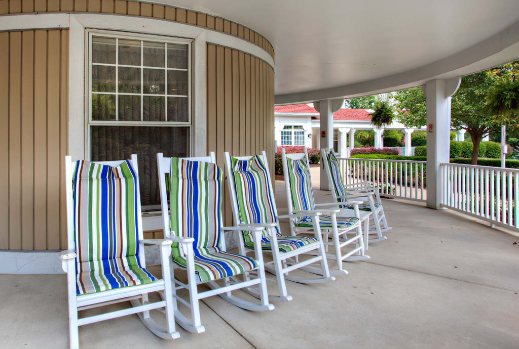 A row of colorful striped rocking chairs on a covered porch.