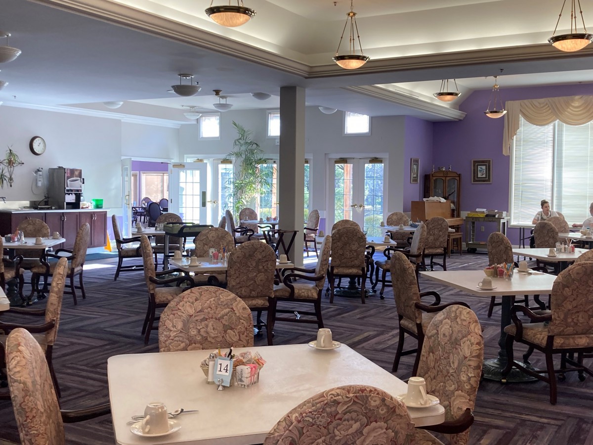 A spacious dining hall with multiple tables and chairs, featuring elegant lighting and decor.